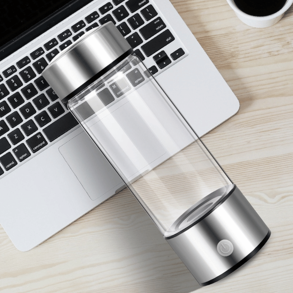 Clear and silver water bottle on a desk with a laptop and coffee cup in the background